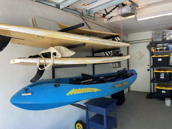 Een kajak met de aanduiding 'Ocean Kayak Malibu Two' en een surfplank in een opslagruimte.
