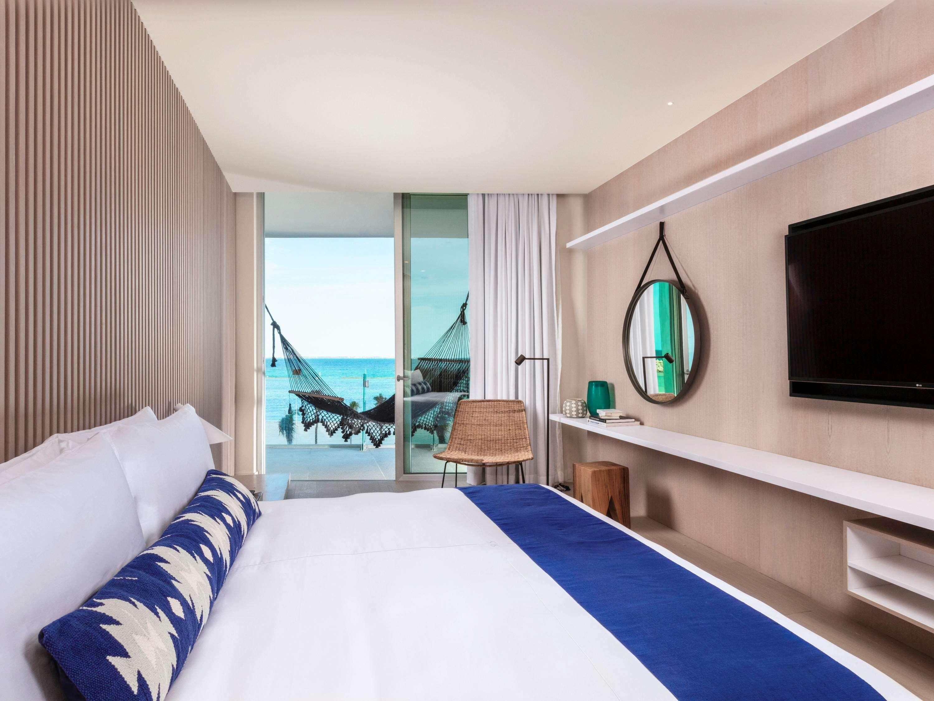 Ein Hotelzimmer mit Bett, Fernseher, Spiegel und Blick auf den Ozean.