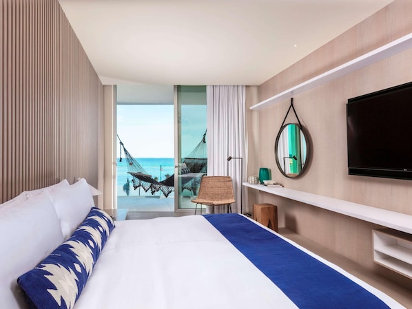 A hotel room with a bed, a TV, a mirror, and a view of the ocean. - SLS Cancun (Cancun)