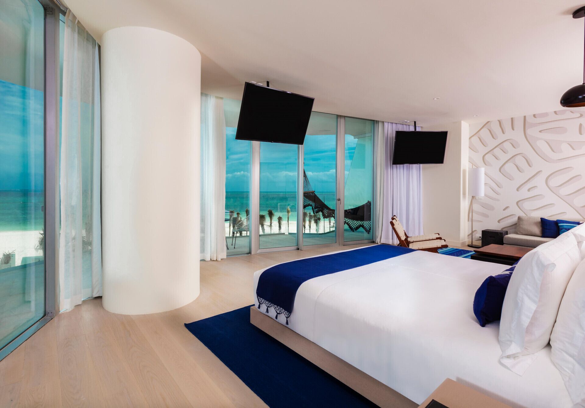 A hotel room with a large bed, a TV, and a view of the beach.