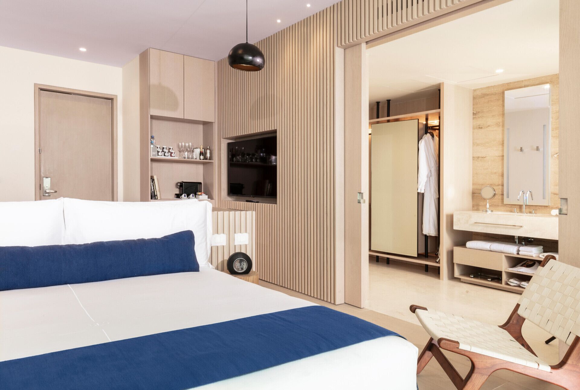 Quarto de hotel moderno com uma cama grande, televisão, guarda-roupa e casa de banho com espelho e lavatório.