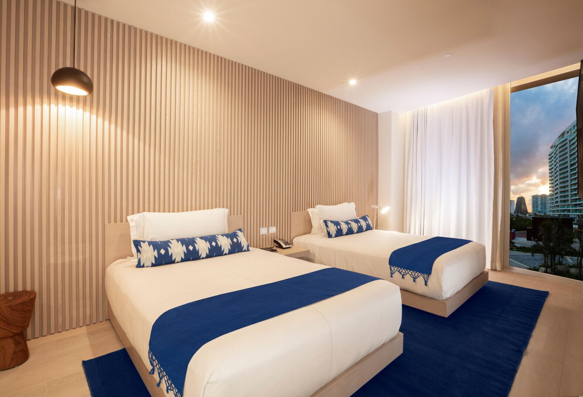 A hotel room with two beds, a city view, and a modern design.