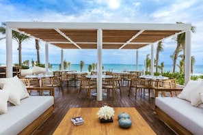 An outdoor seating area with tables and chairs, a wooden deck, and a view of the ocean.