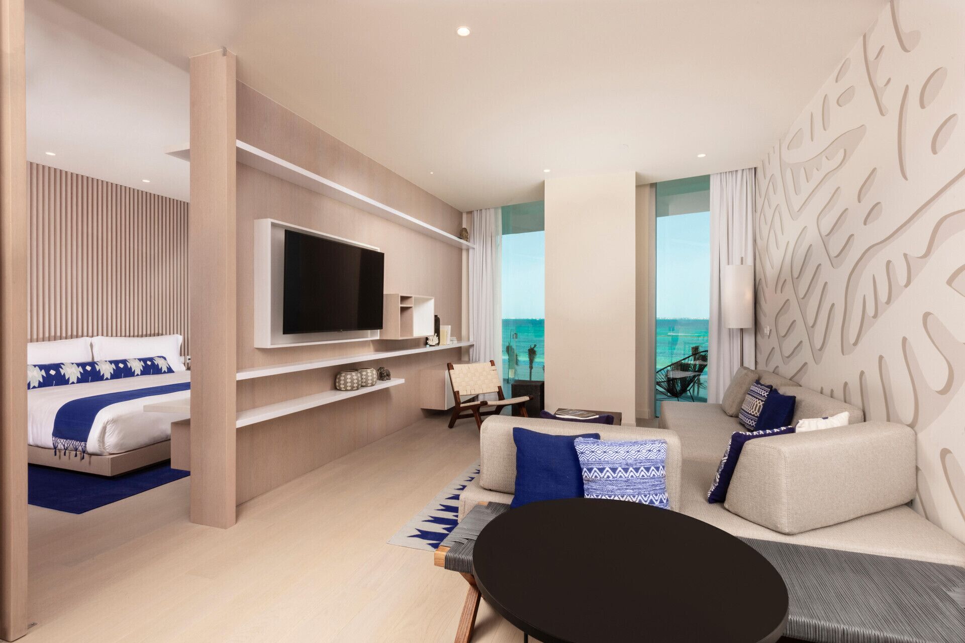 A modern hotel room with a bed, a TV, a sofa, a coffee table, and a view of the ocean.