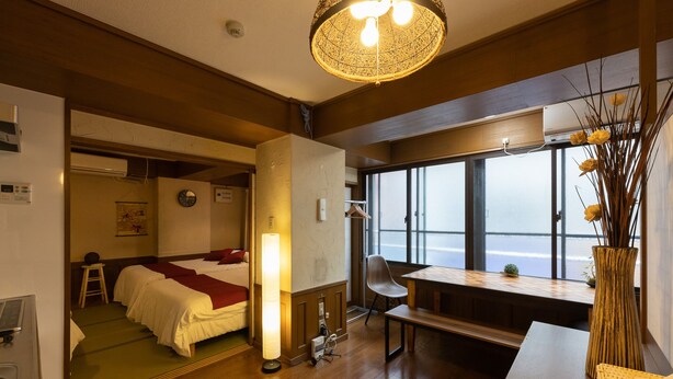 A hotel room with a bed, bedside table, lamp, chair, and a view of the sea through large windows. - Yoneyama 2F (Osaka)