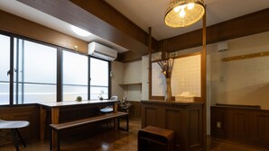 A room with wooden flooring, a bench, a table, a hanging light fixture, and a window with an air conditioning unit. - Yoneyama 2F (Osaka)