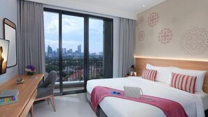 Ein Hotelzimmer mit einem großen Bett, einem Schreibtisch mit Stuhl, Blick auf die Stadt und einem Balkon.
