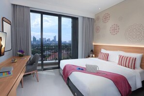 A hotel room with a large bed, a desk with a chair, a view of the city, and a balcony.