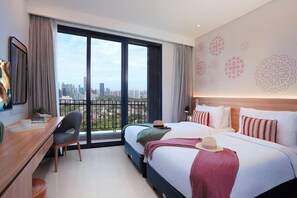 A hotel room with a large window, a desk, a bed with pillows, and a wall with decorative patterns. - Citadines Gatot Subroto Jakarta (JAKARTA)