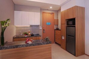 A modern kitchen with a marble countertop, wooden cabinets, a built-in microwave, and a refrigerator. - Citadines Gatot Subroto Jakarta (JAKARTA)