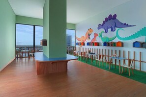 A children's play area with a large window, a wooden play table, and colorful dinosaur wall art. - Citadines Gatot Subroto Jakarta (JAKARTA)