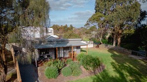 A modern house with a covered patio, surrounded by a well-maintained lawn and mature trees. - Bluelake Cottage Metung (Metung)
