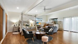 A spacious living room with a four-poster bed, a ceiling fan, and a large TV. - Bluelake Cottage Metung (Metung)