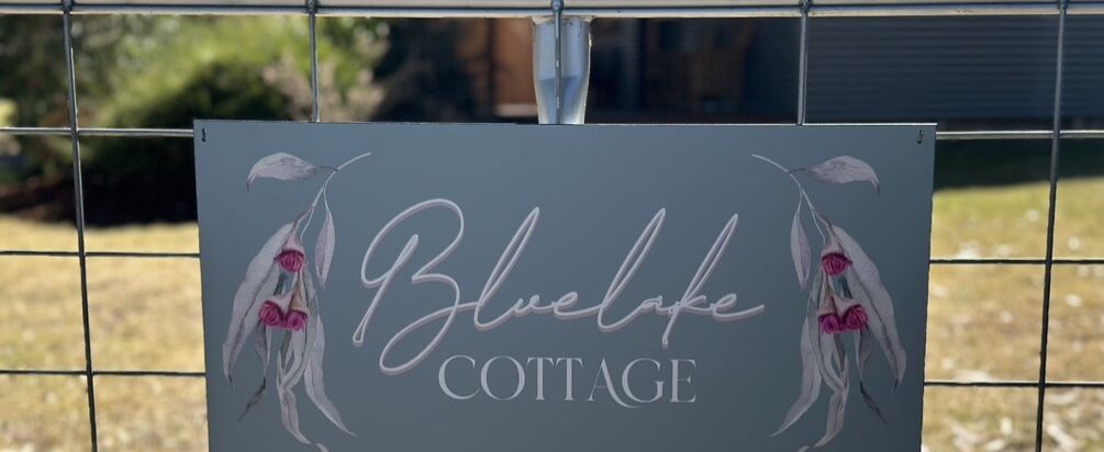 A sign for Blue Lake Cottage with a floral design.