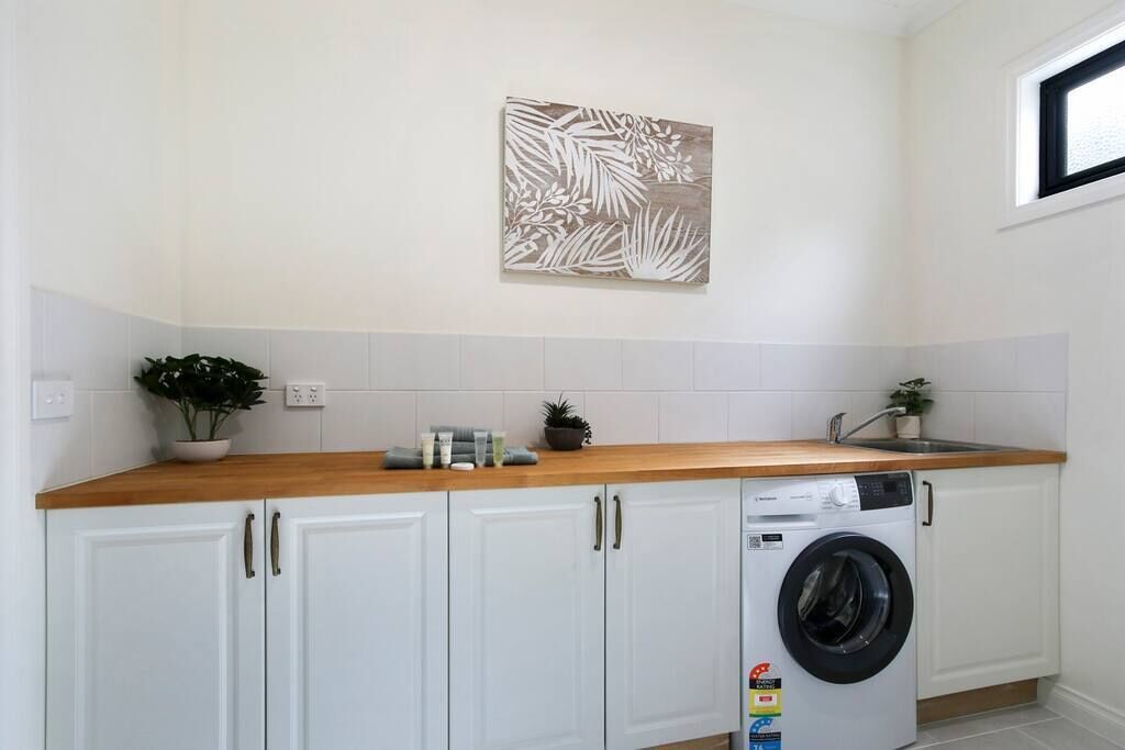 Un cuarto de lavado con lavadora, gabinetes blancos, encimera de madera y una obra de arte colgada en la pared.