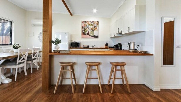 A modern kitchen with white cabinets, a wooden countertop, and three bar stools. - Bluelake Cottage Metung (Metung)