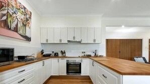 A modern kitchen with white cabinets, a wooden countertop, and a built-in oven. - Bluelake Cottage Metung (Metung)