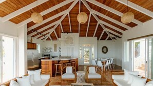A spacious living area with a high wooden ceiling, a central island with seating, and a view of the kitchen and dining area. - Villa Magli (Christiansted)