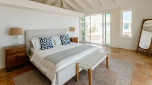 A bedroom with a large bed, wooden nightstands, a bench, and a ceiling fan. - Villa Magli (Christiansted)