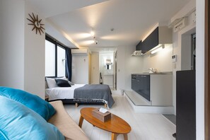 A compact hotel room with a bed, a sofa, a wooden coffee table, a kitchenette, and a bathroom visible through an open door. - Yoneyama 3F (Osaka)