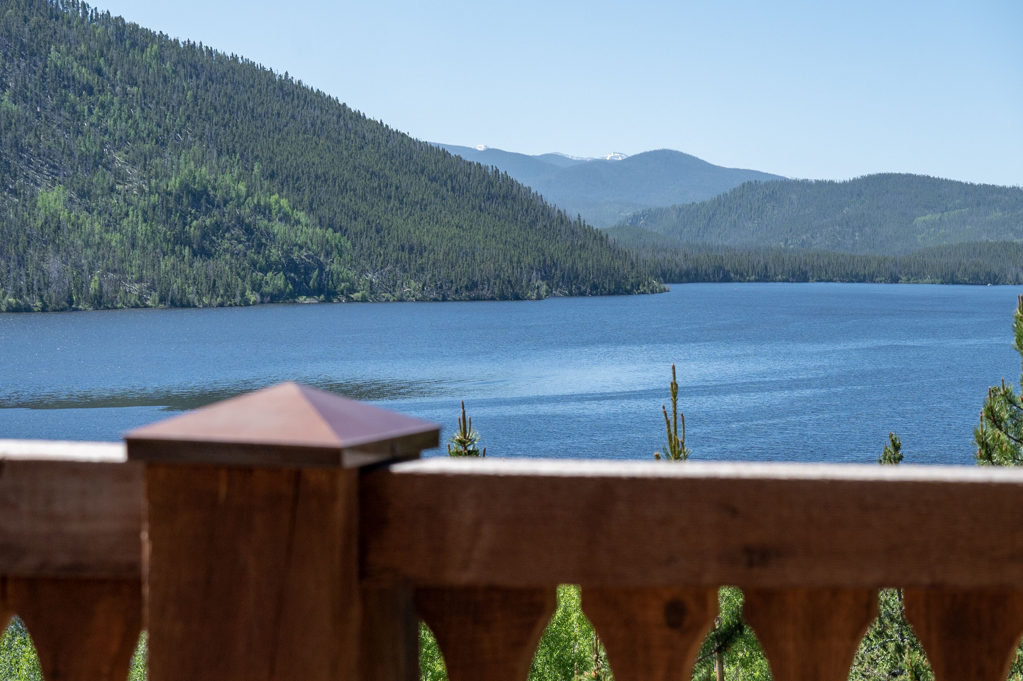 Una terraza de madera con vista a un lago tranquilo y colinas boscosas en el fondo.
