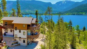 A two-story lodge with a balcony overlooking a lake, surrounded by forest and mountains. - Swiss Chalet: Hot Tub, EV Charger, Lake Views (Grand Lake)