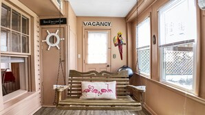 A room with a wooden bench, a hammock, a 'VACANCY' sign, a ship's wheel decoration, and a 'Above all, have a good time' sign.