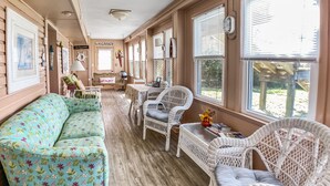 A spacious room with a large floral sofa, white wicker chairs, and a wooden floor.