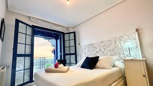 Un dormitorio con cama, mesita de noche, ventana con cortinas y vistas al exterior.
