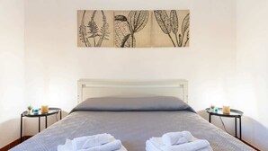 Una cama bien hecha con toallas blancas dobladas, un cabecero blanco y una obra de arte en la pared superior.