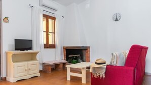 Una sala de estar con televisión sobre un mueble, chimenea, sillón rojo y un reloj en la pared.
