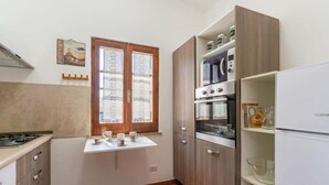 Cocina compacta con estufa a gas, horno y microondas integrado. Hay una ventana con vidrio esmerilado y una pequeña mesa con tazas.