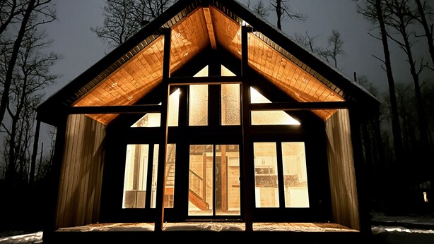 Eine Holzhütte mit großen Fenstern und einem geneigten Dach, umgeben von Schnee und Bäumen.