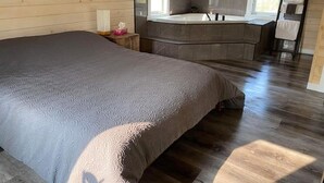 Ein Schlafzimmer mit einem großen Bett, Holzboden, dunkler Wand, einem Fenster und einem Badezimmer mit einer Badewanne.