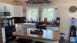 Eine moderne Küche mit weißen Schränken, einer Holz-Kochinsel mit zwei Hockern, einem Edelstahl-Kühlschrank und einer Kaffeemaschine.