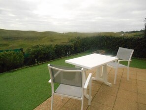 A patio with a white table and two chairs, surrounded by a well-maintained lawn and hedges, with a view of rolling hills in the distance. - Appartement Face MER (Bretignolles-sur-Mer)