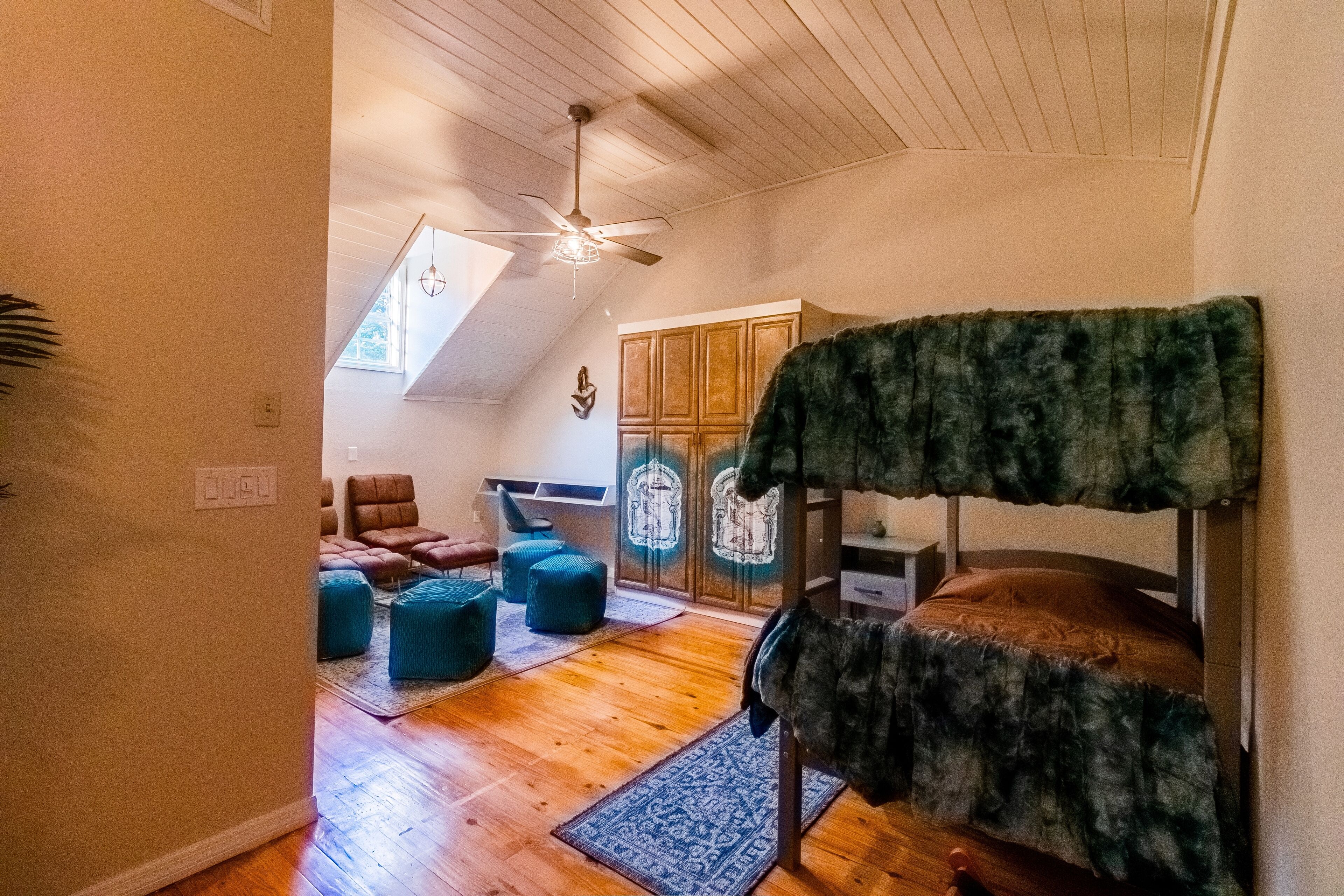 Ein gemütliches Zimmer mit Etagenbett, Holzboden, Deckenventilator und Blick auf eine Holztür und einen Stuhl.