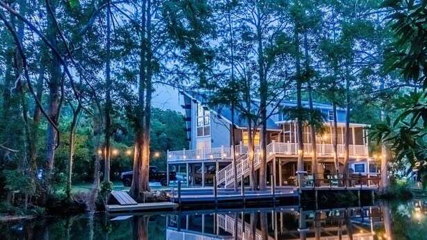 A waterfront property with a multi-level deck, surrounded by trees and a calm body of water. - Waterfront Retreat + Kayaks - Extended Stay Deal (Spring Hill)