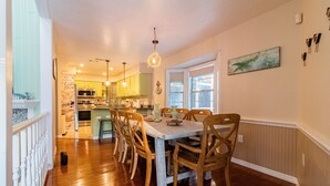 A dining area with a wooden table and chairs, a chandelier, and a view of the kitchen in the background. - Waterfront Retreat + Kayaks - Extended Stay Deal (Spring Hill)