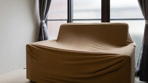 A room with a single beige chair near a window with curtains, a plain wall, and a visible window frame. - Yoneyama 4F (Osaka)