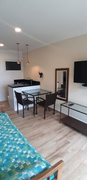 A modern room with a bed, a dining table with chairs, a small kitchen area, and a TV mounted on the wall.