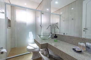 A modern bathroom with a glass sink, a toilet, and a shower area.