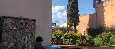 A swimming pool with a stone wall and a tall tree in the background.