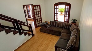 A living room with a wooden staircase, a sectional sofa, and a potted plant by the window. - Casa com Piscina e Churrasqueira (Foz do Iguaçu)
