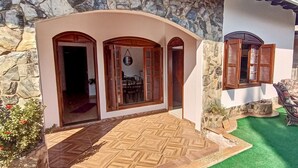 A house with a stone facade, wooden doors, and a patio with outdoor furniture. - Casa com Piscina e Churrasqueira (Foz do Iguaçu)