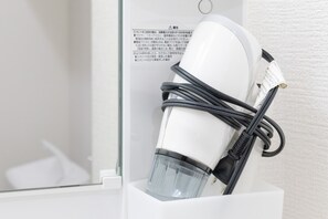 A white hair dryer with a transparent water bottle attached to it, placed on a white surface with a warning label in the background. - Yoneyama 5F (Osaka)