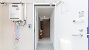 A hallway with a water heater, a door with a handle, and a small shelf with items. - Yoneyama 5F (Osaka)