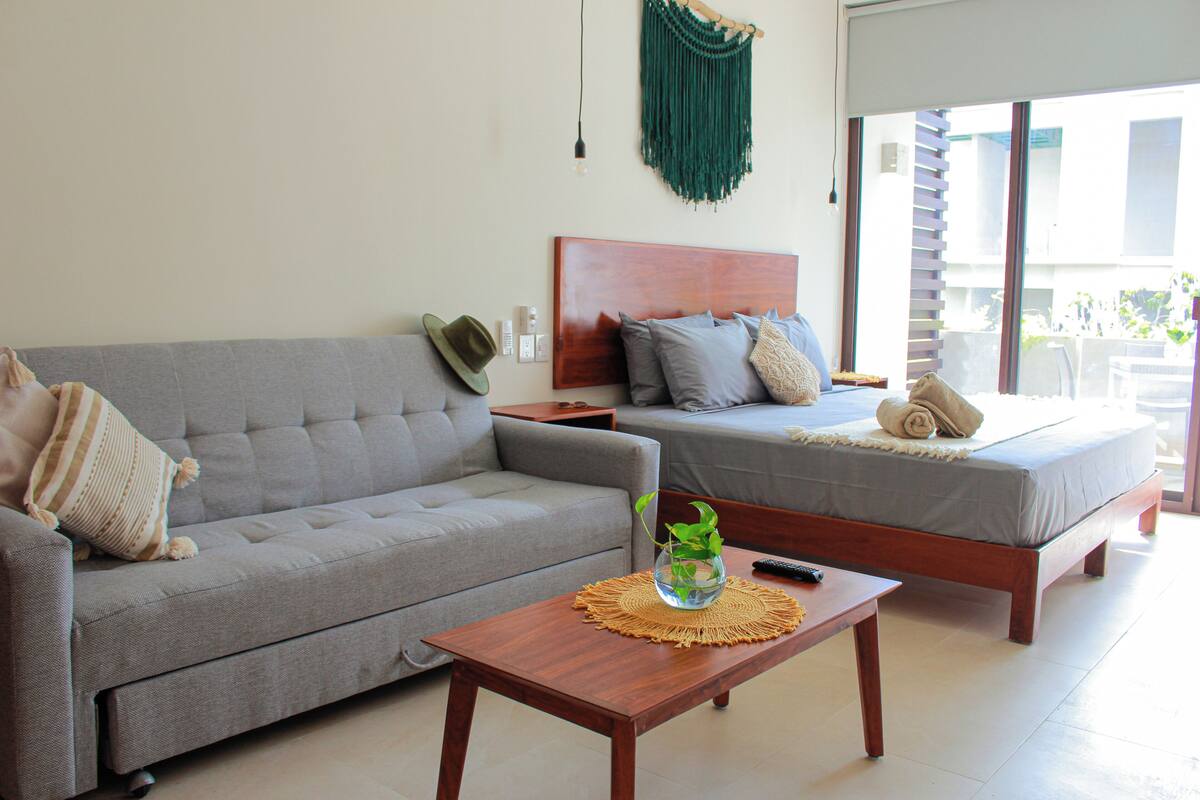 A modern bedroom with a grey sofa, a wooden nightstand, a bedside table, and a bed with a wooden headboard.