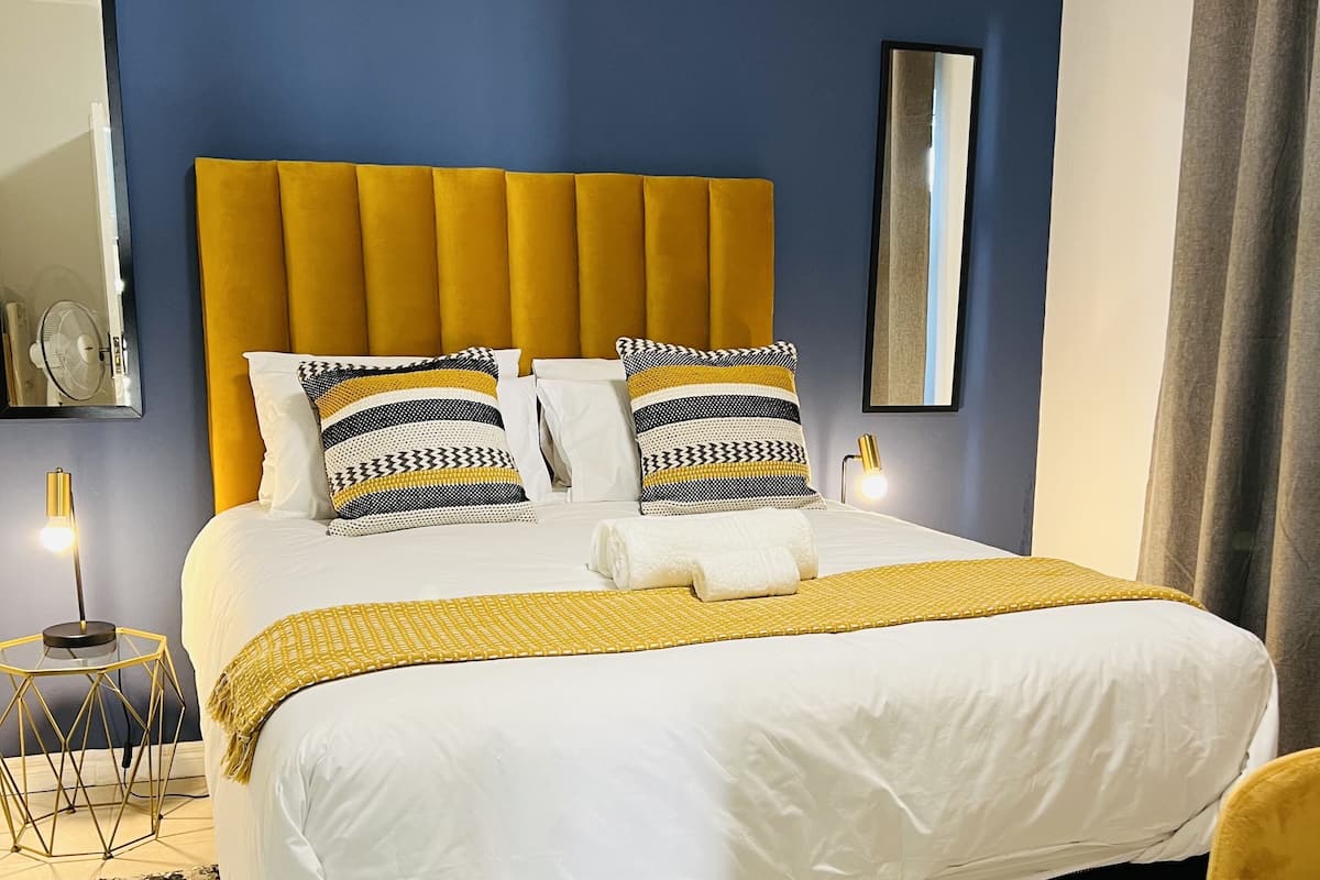 A neatly made bed with a yellow headboard, white bedding, and patterned pillows.