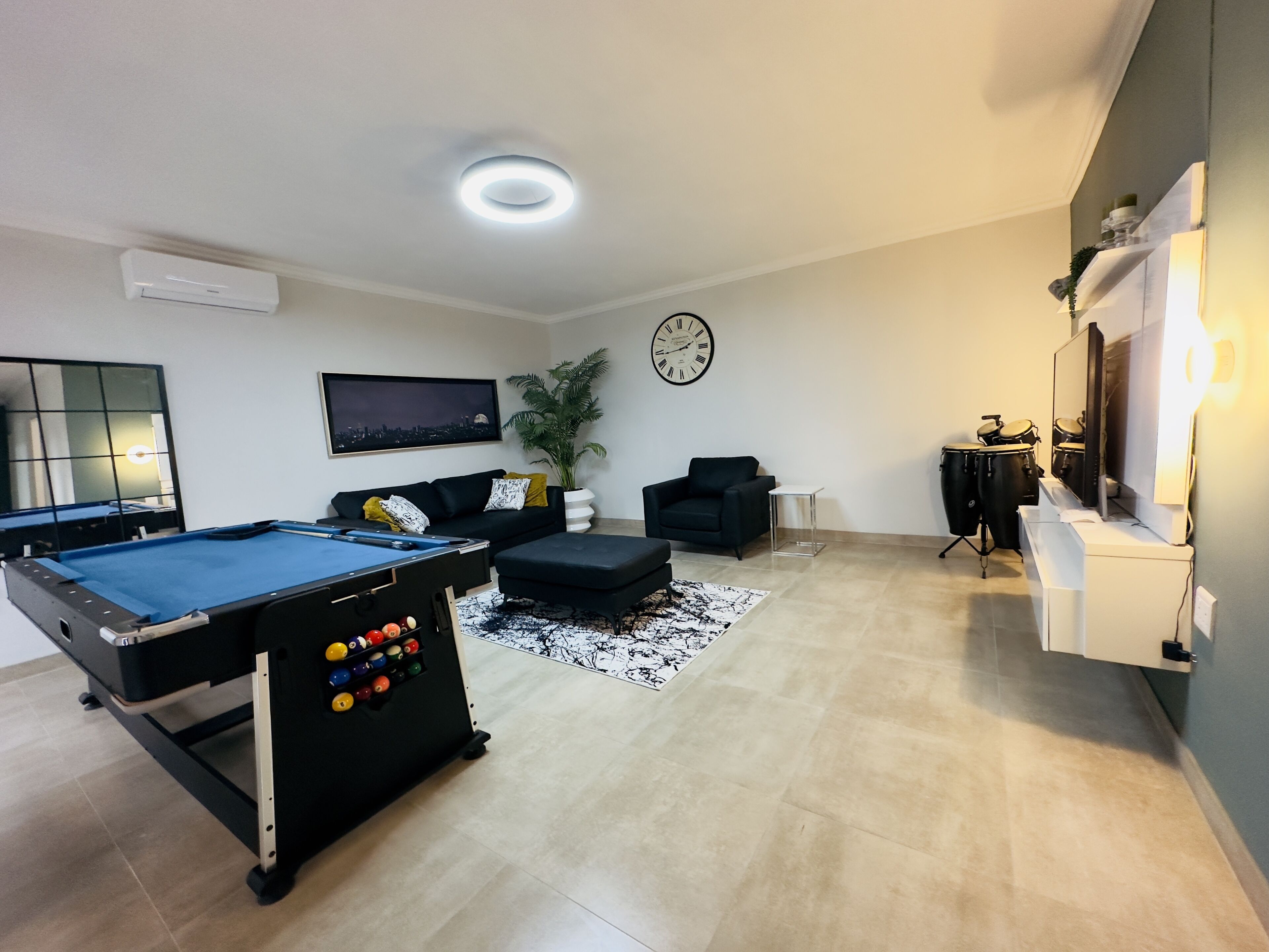 A modern living room with a pool table, a comfortable sofa, a coffee table, a potted plant, and a drum set.
